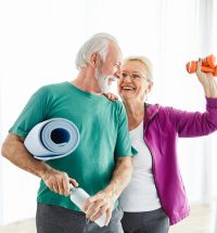 Portrait of a senior couple  holding water bottle and exercise mat smiling and posing at home healthy living